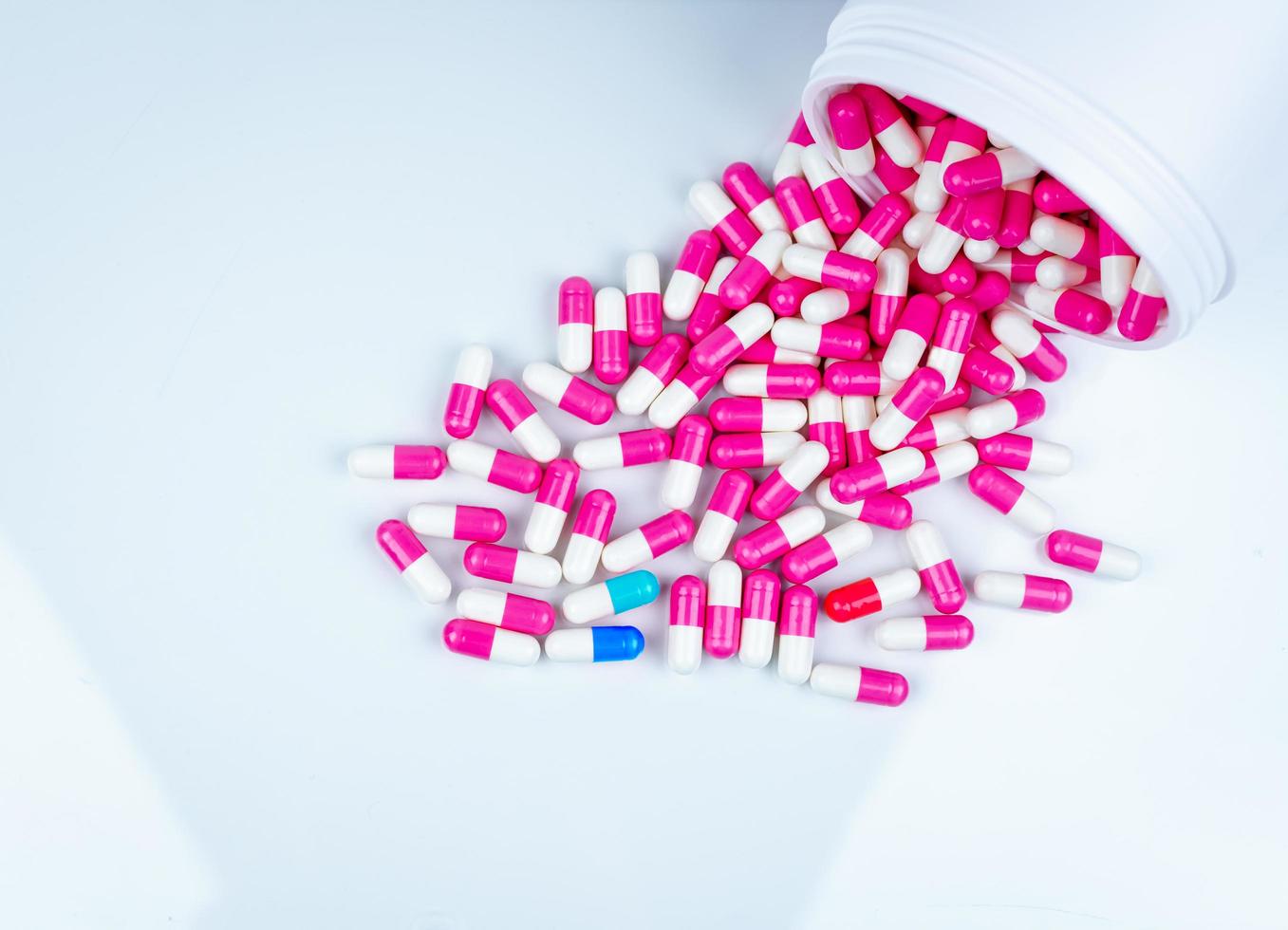 Blue-white capsule contaminated in pink-white capsule pills. Capsule pills spread out of plastic drug bottle. Pharmaceutical industry. Pharmacy drugstore background. Antibiotic drug use in hospital. photo