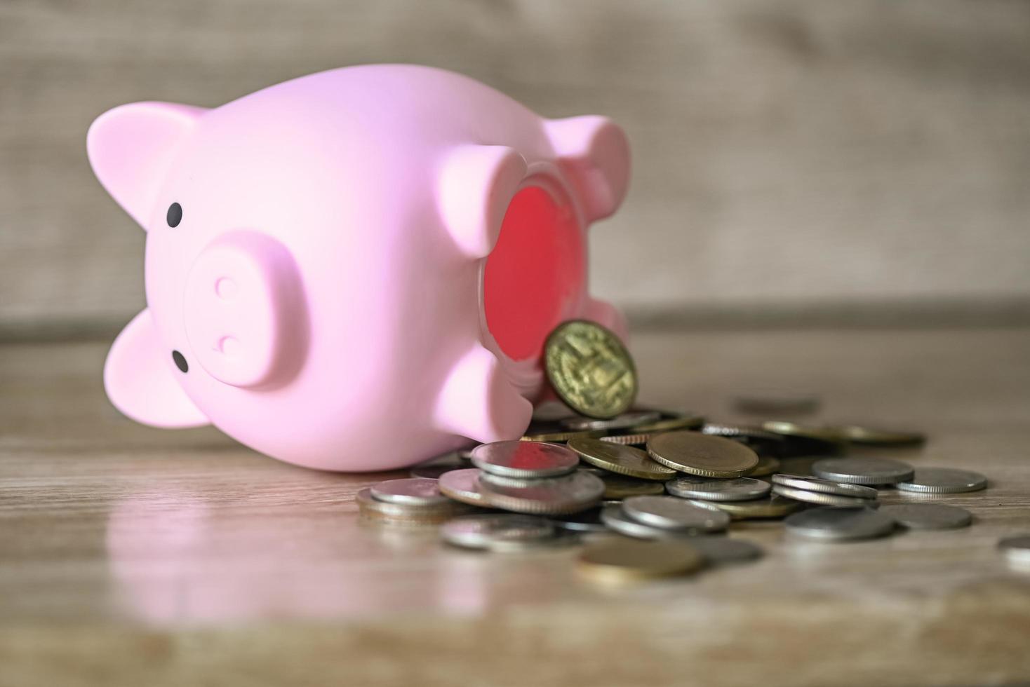 Broken piggy bank with and coins on wooden background, saving money for education study or investment concept photo