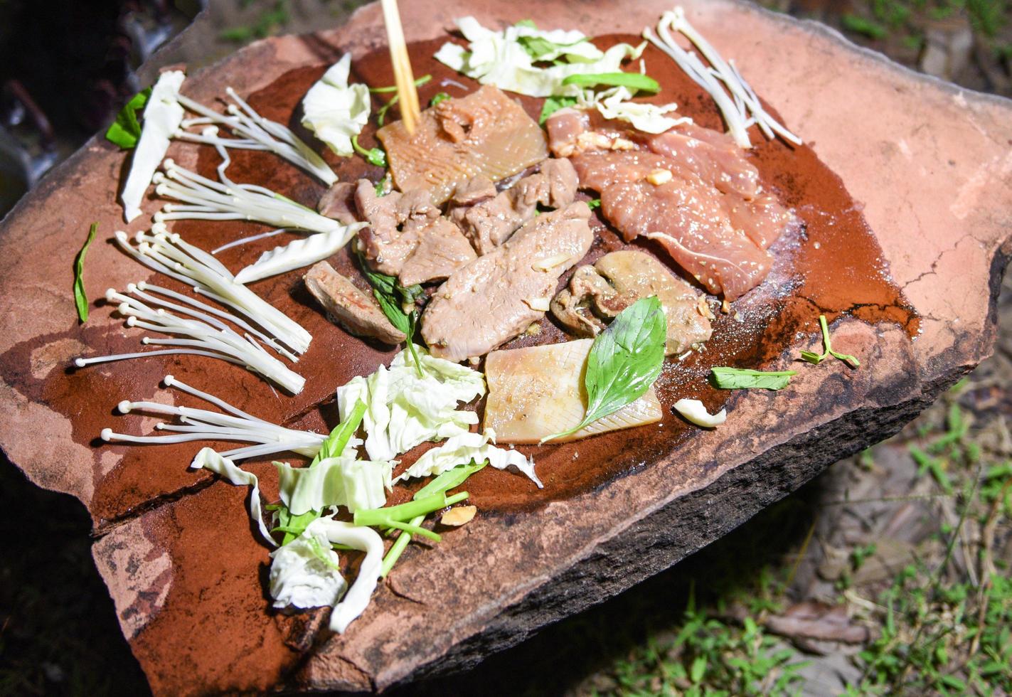 Food on stone - shabu shabu grilled pork meat and vegetables and mushrooms on hot stone plate , Survival in the wild concept photo
