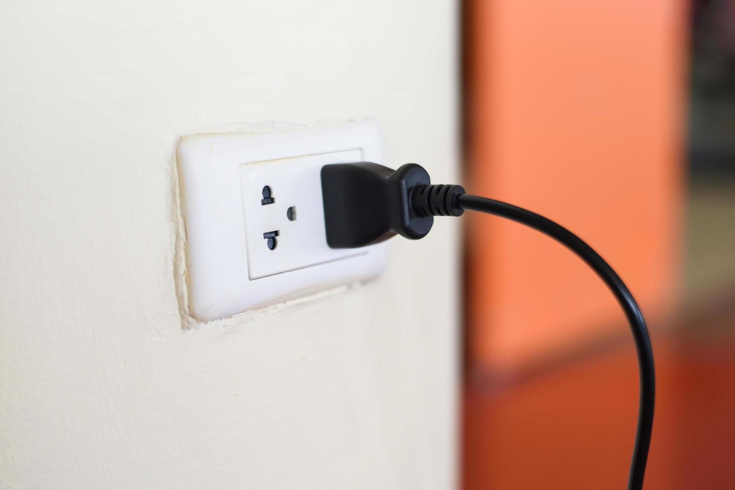 Home outlet plug is plugging socket on wall with black power cord cable - Power plug connecting electrical plug photo