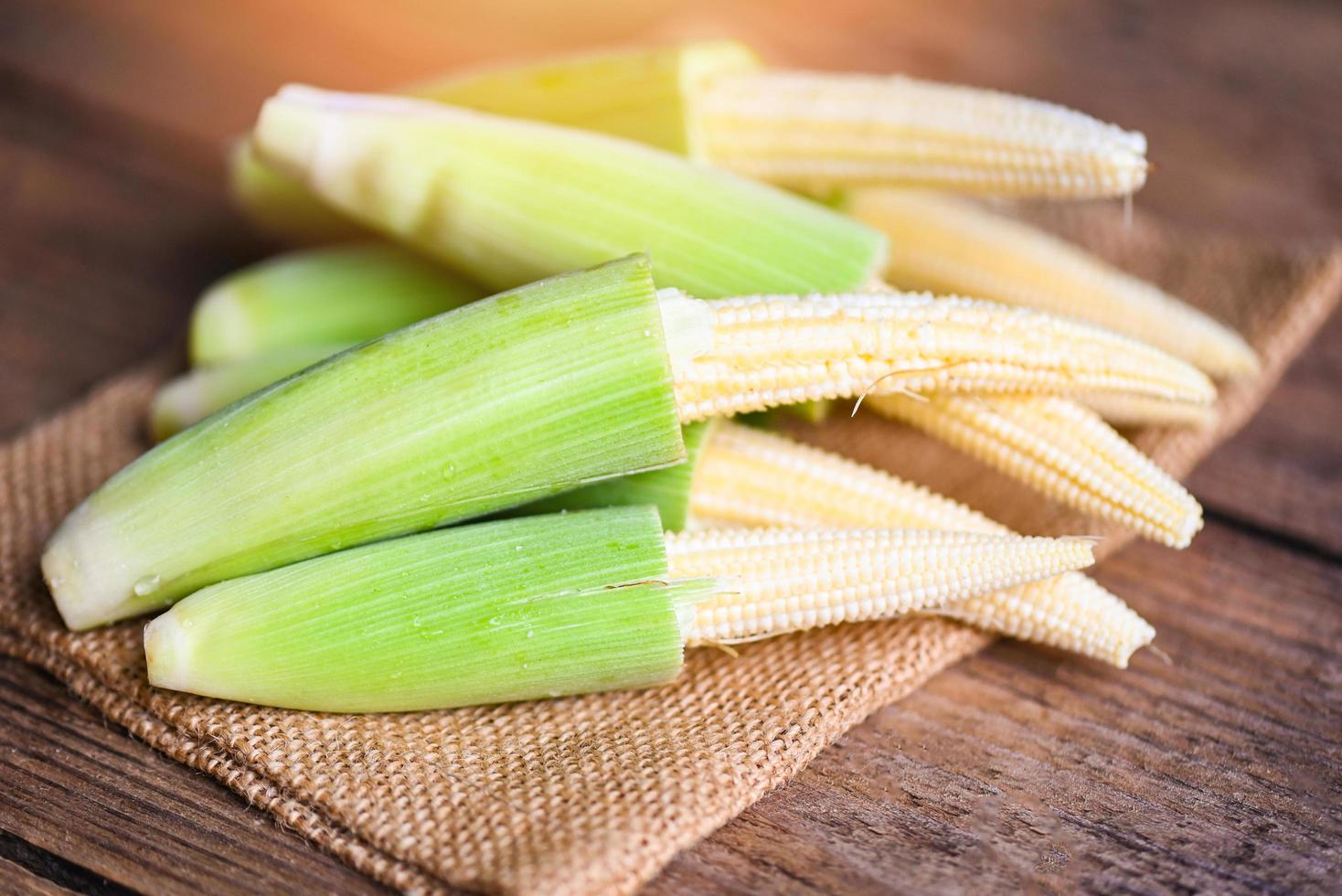 Baby corn on the sack, Fresh young baby corn for cooking health food, Close up raw organic baby corn on wooden background. photo