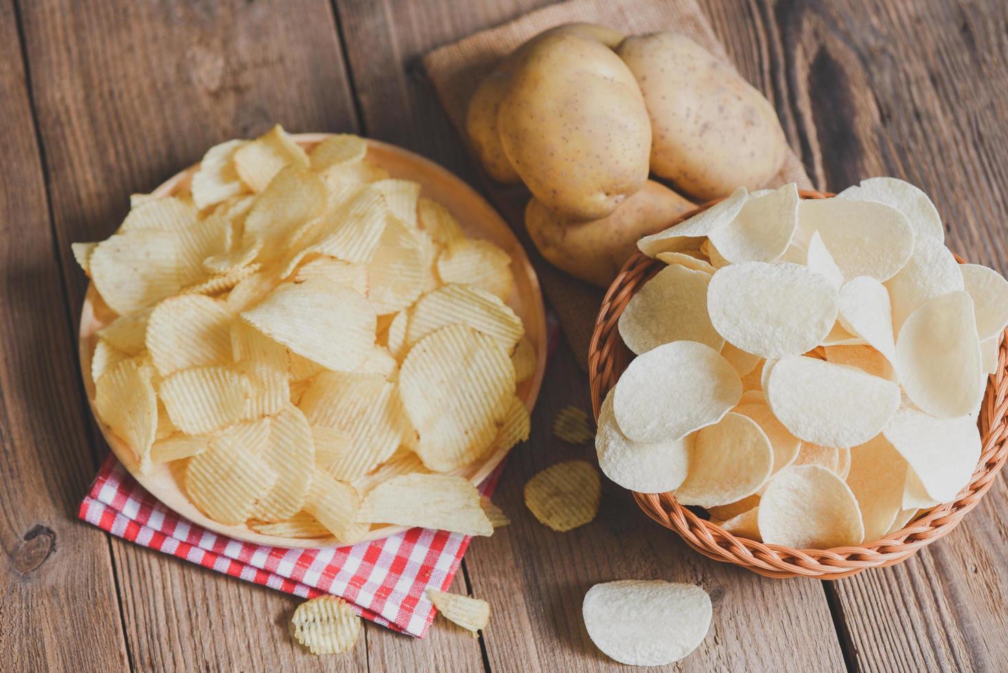 Crispy potato chips on the kitchen table and fresh raw potatoes on wooden background, Potato chips snack on bowl and plate photo