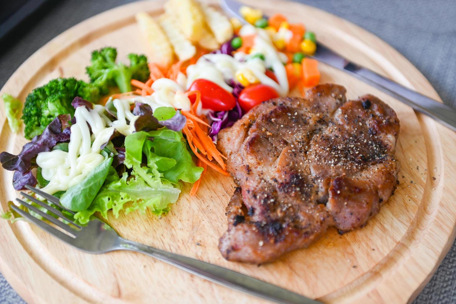 bistec casero con patatas fritas y ensalada de verduras frescas en bandeja de madera, menú de bistec saludable, bistec de cerdo foto