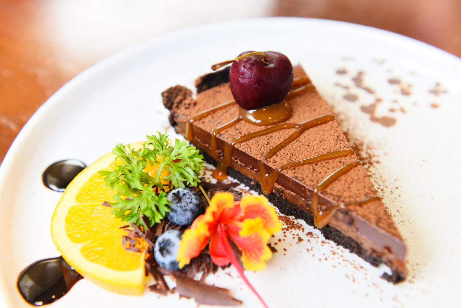 Pastel de chocolate con caramelo de cereza y fruta en la placa blanca - Cerrar la rebanada de pastel foto