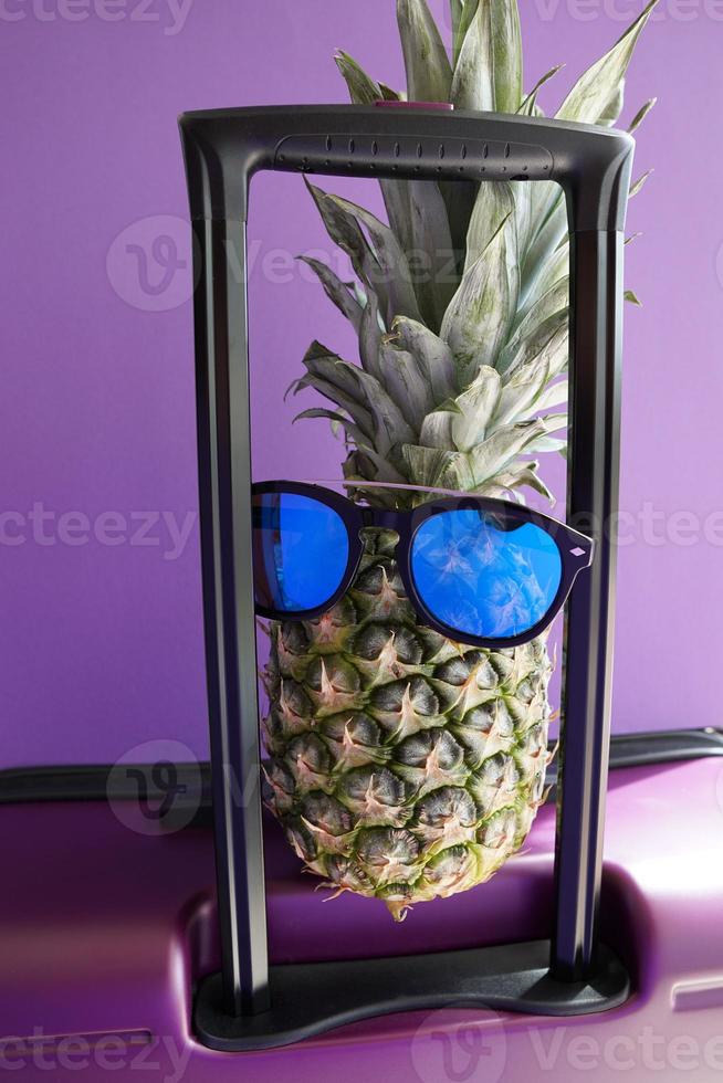 piña en las gafas de sol azules en la maleta de viaje. foto