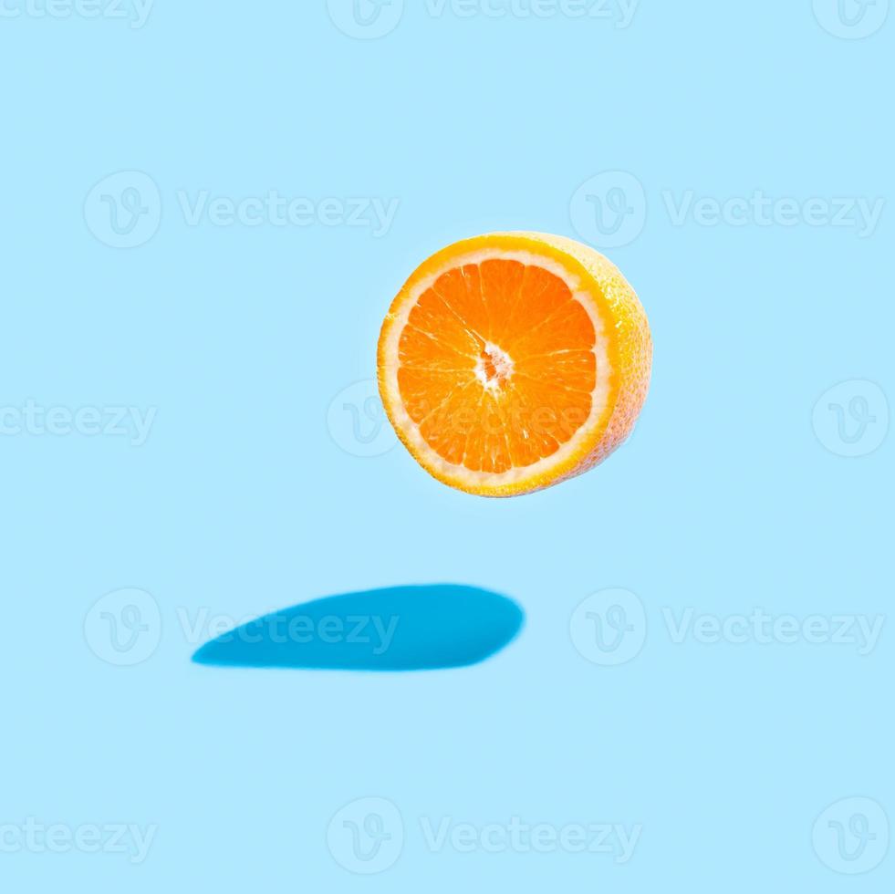 Isolated orange half with a real shadow on blue background. Flying orange on blue. photo