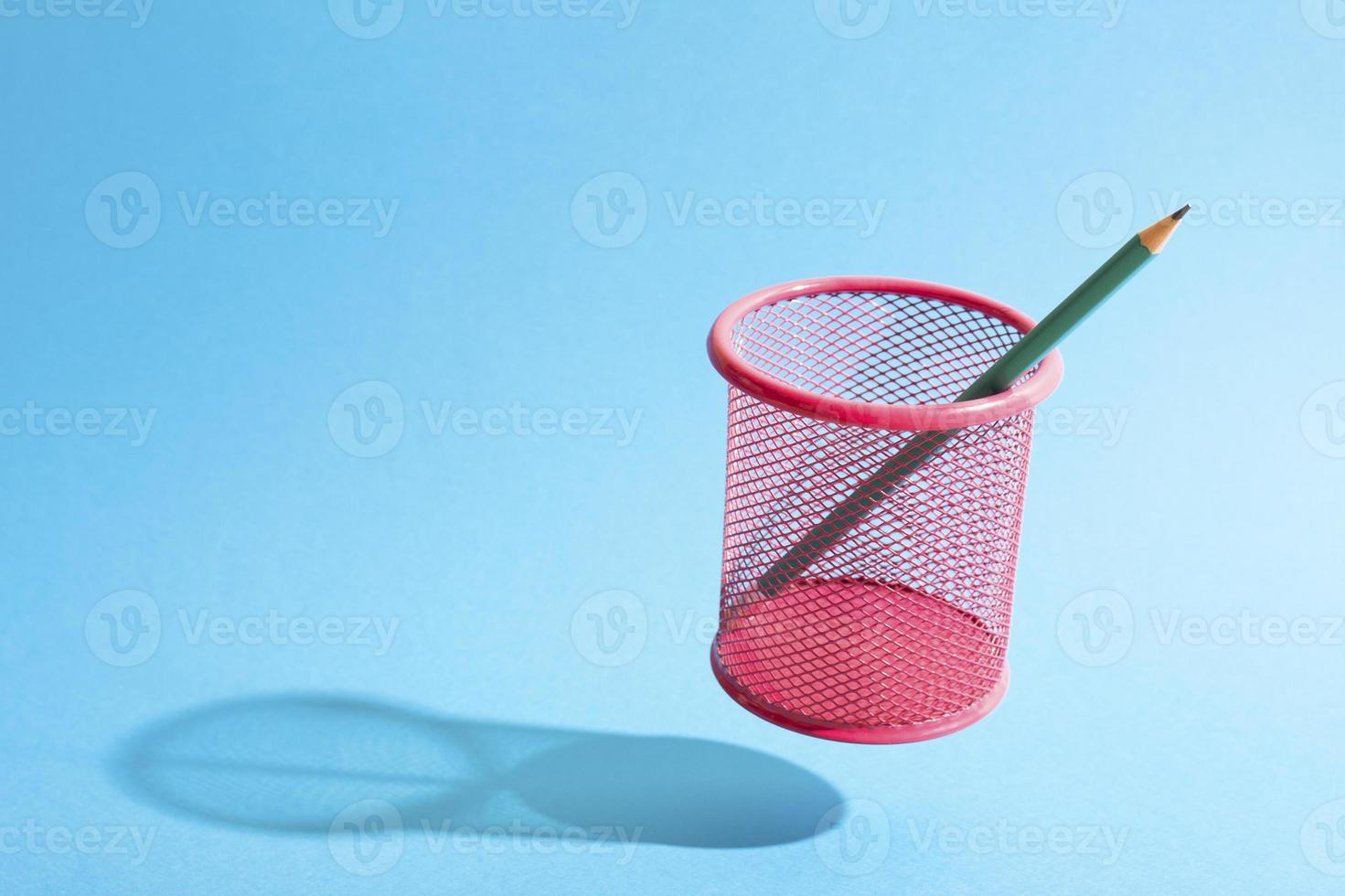 A pencil on a flying fink mesh pencil cup on blue background. photo