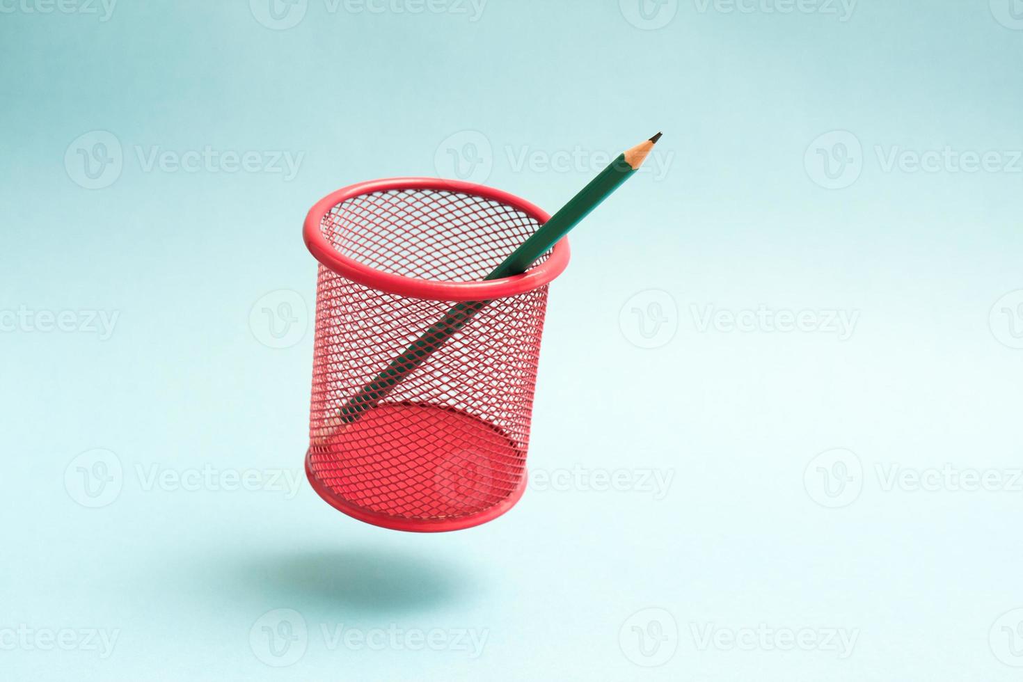 Flying red mesh pencil cup with a single pencil. Green pencil in a flying cup. photo