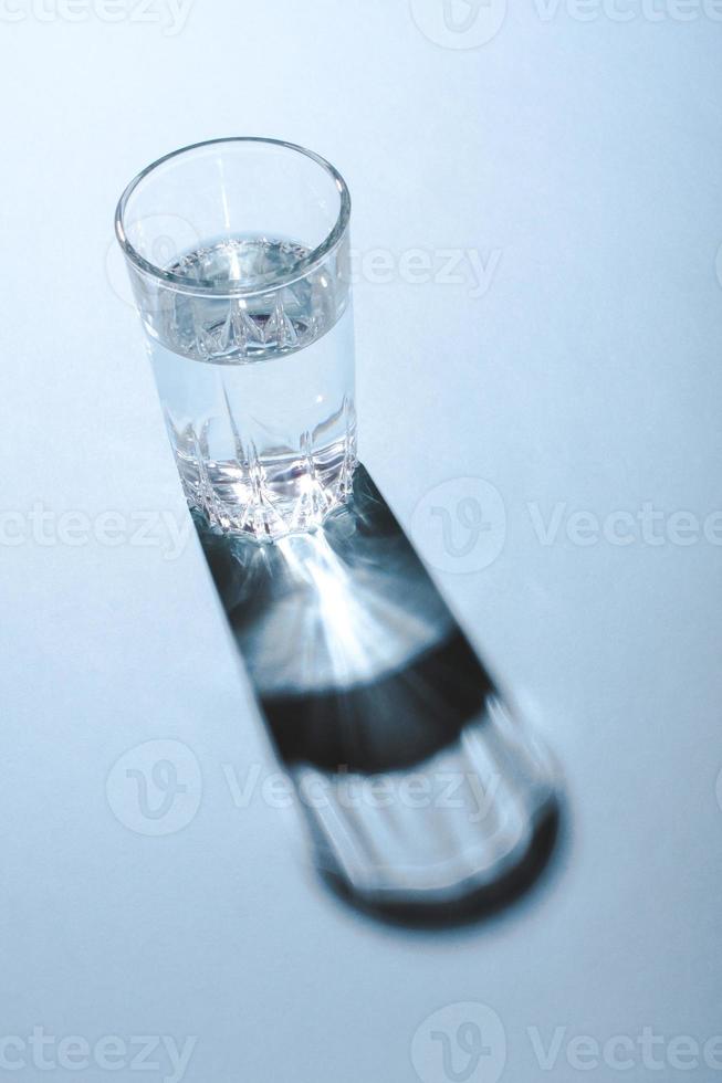 Glass of clean water under the bright light throwing a hard shadow on blue background. photo