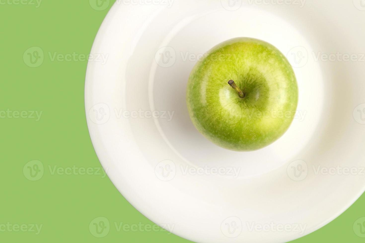 Green apple on white plate. Simple healthy lifestyle flat lay with an apple on a plate. photo