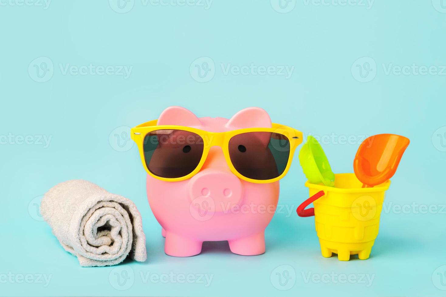 Summer holiday concept.Pink piggy money bank with beach towel,sunglasses and beach bucket photo