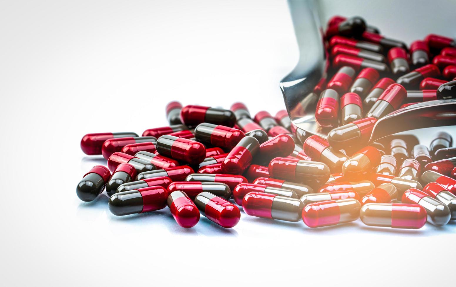 Red and gray capsule pills on stainless steel drug tray and some capsule pills on white background. Pharmacy drugstore product. Capsule pills count. Pharmaceutical industry. Healthcare and medicine. photo