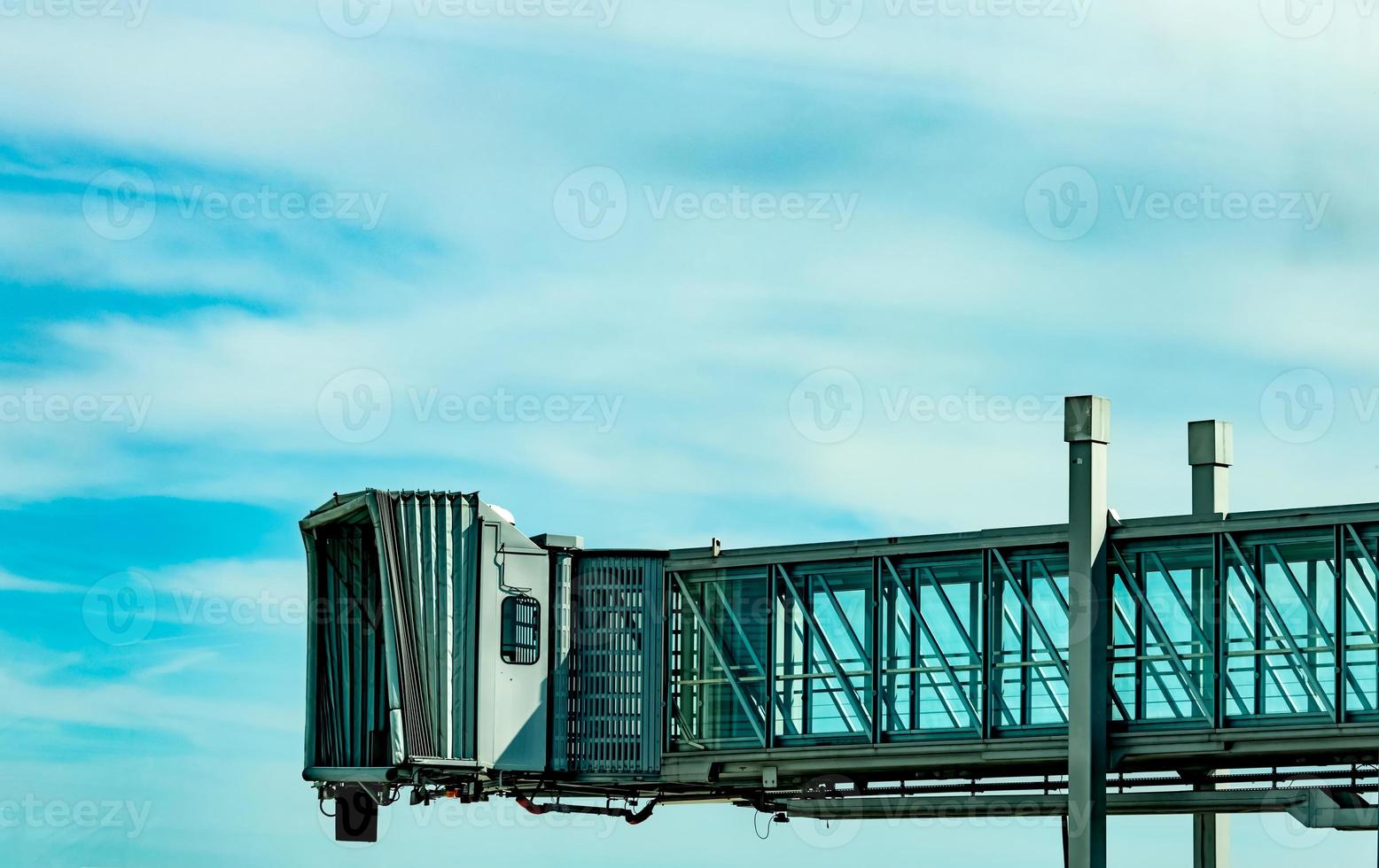 jet bridge después de que la aerolínea comercial despegue en el aeropuerto contra el cielo azul y las nubes blancas. puente de embarque de pasajeros de aviones acoplado. vuelo de salida de la aerolínea internacional. puente de chorro vacío. foto