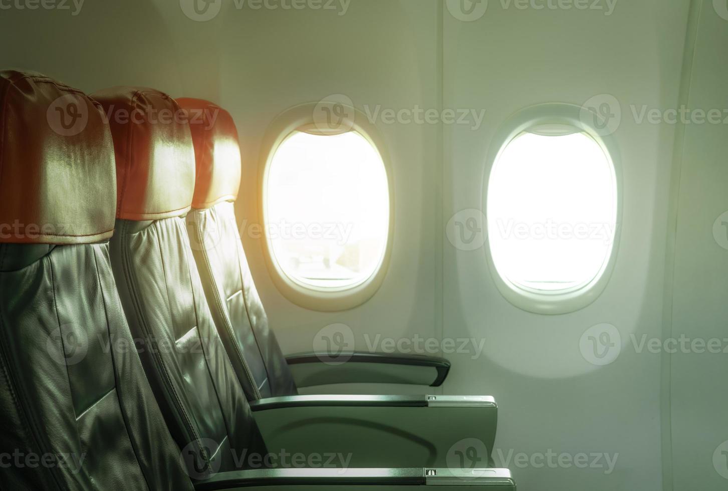 Empty airplane seat economy class in the cabin of the commercial airline. Cheap plane seat with windows and sunlight. Passenger chair in economy flight. Airplane cabin interior. Leather seat aircraft. photo