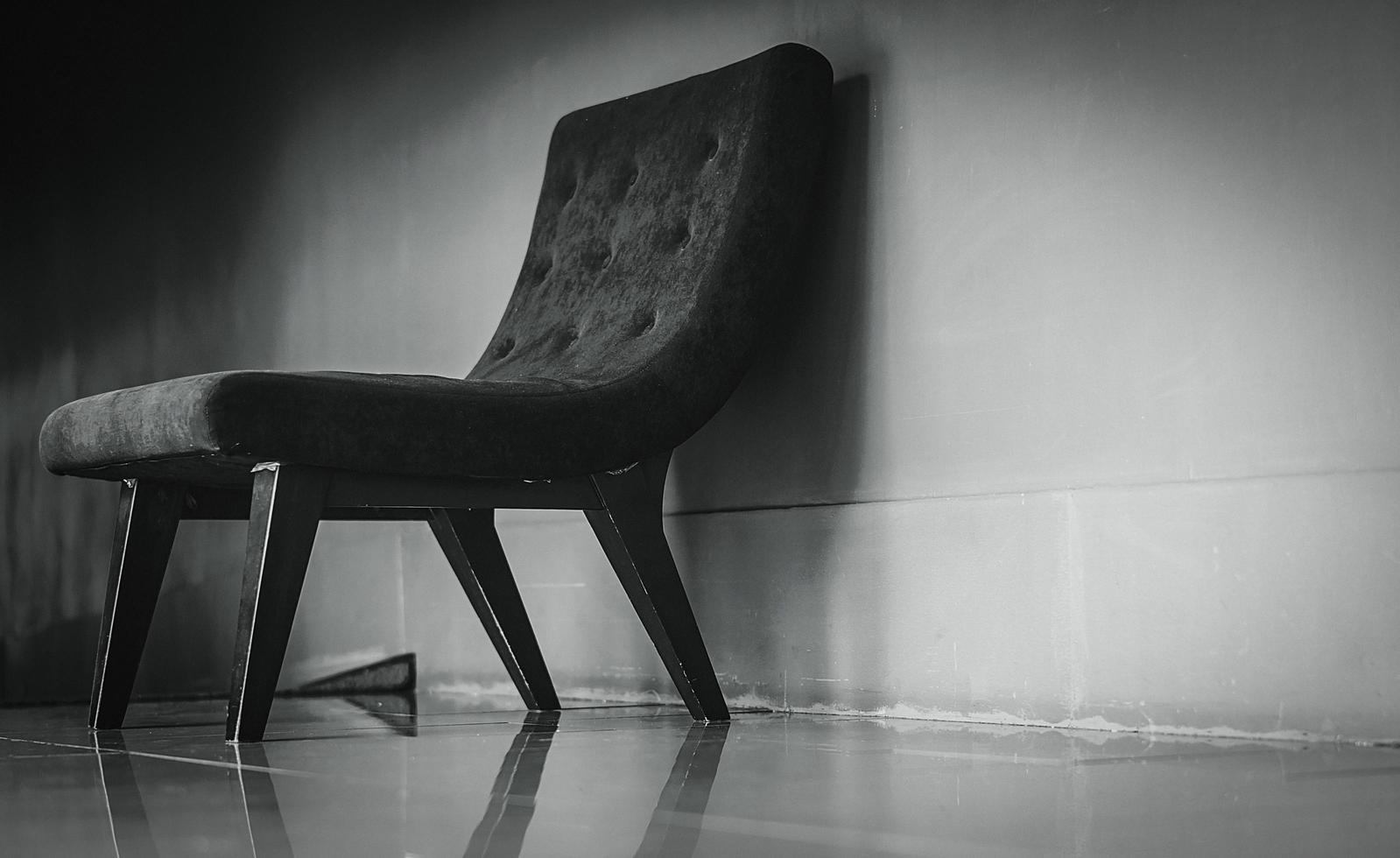 Black classic chair with unique design in empty rest room near concrete wall on dark and dramatic background. Depressed, sad and lonely concept. One empty armchair in living room. Interior furniture. photo