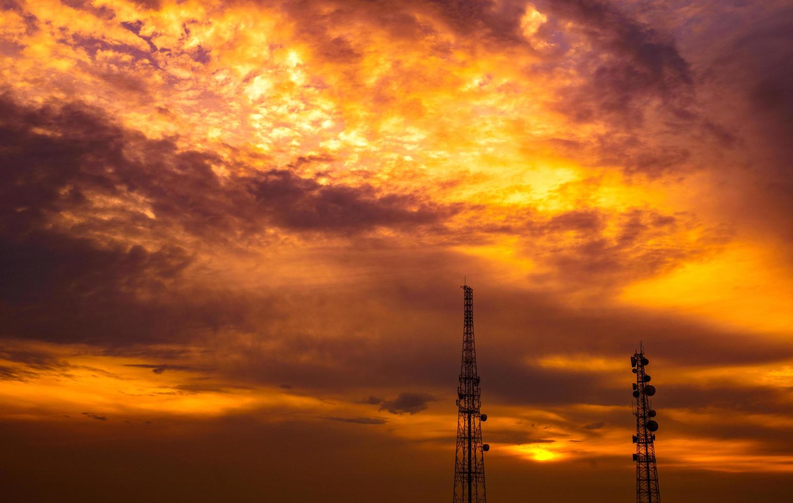 Two telecommunication towers on dramatic dark-orange sky and cumulus clouds background photo