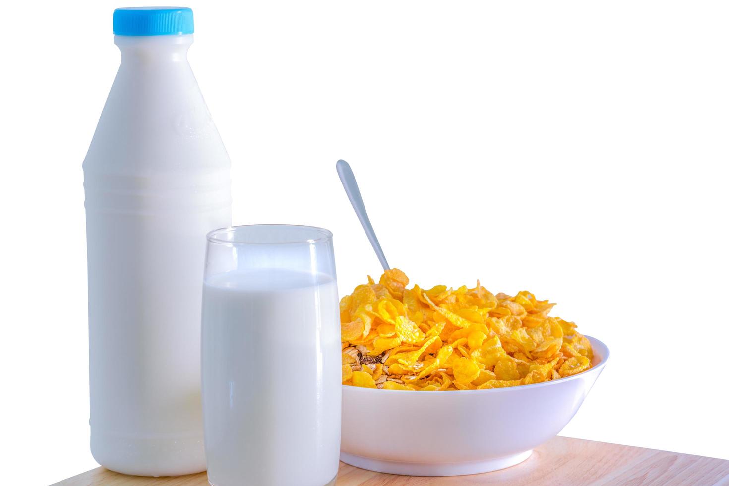 One glass of milk and milk bottle with blank label put on wood table near bowl of cereal with spoon. Calcium food breakfast for children before go to school in the morning. Cornflakes and milk concept photo