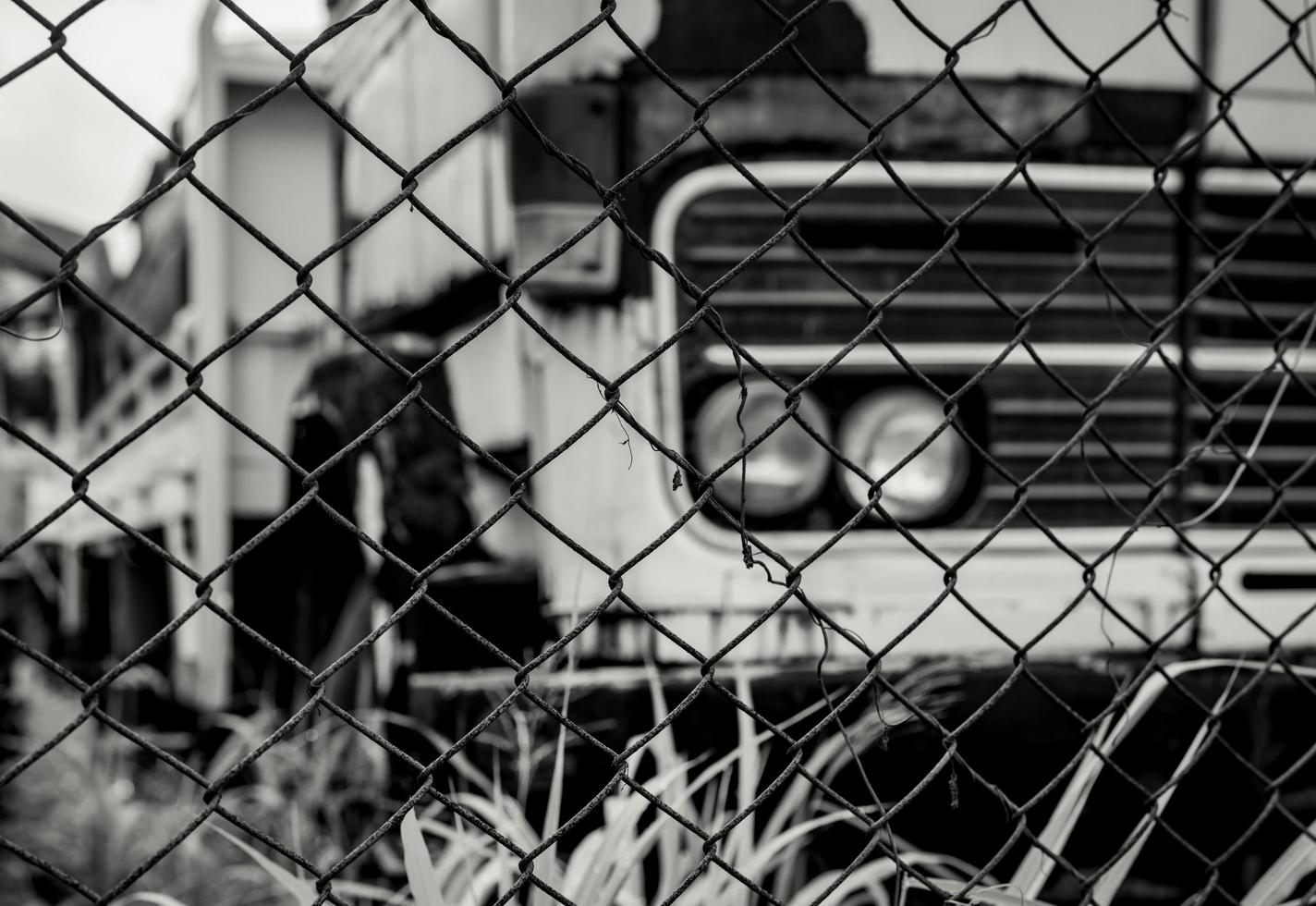 Old wrecked lorries in black and white scene. Abandoned rusty truck in wire fence. Decayed abandoned truck. View from fence to truck. Tragedy and loss. Financial crunch and economic recession concept. photo