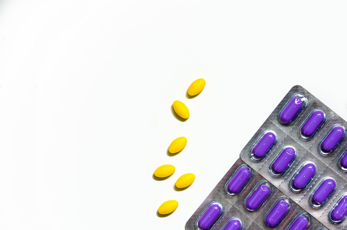 Macro shot of yellow oval tablet pills on white background and purple caplets pills in blister pack. Mild to moderate pain management. Pain killer medicine. Paracetamol and ibuprofen tablet pills. photo