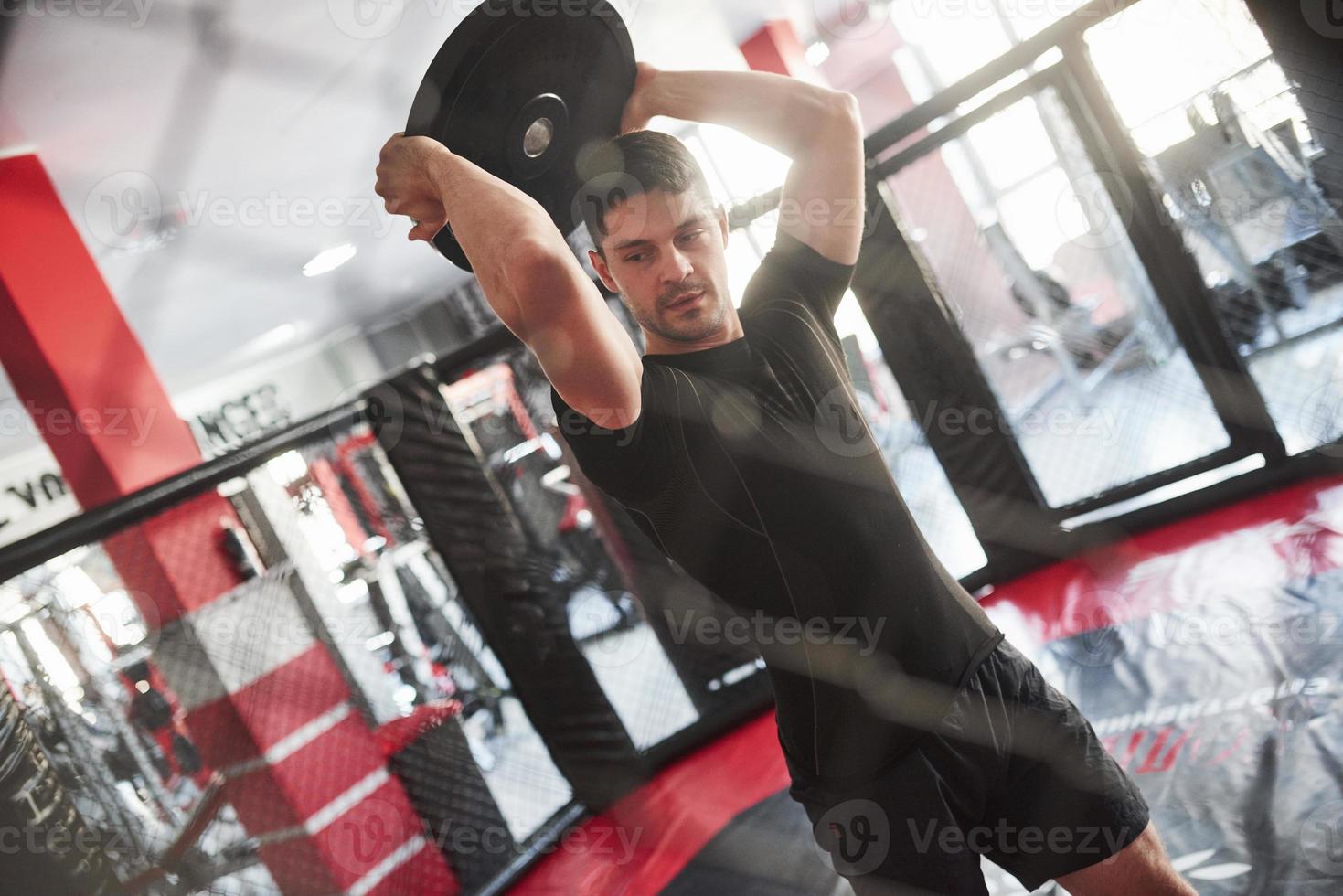Raising up heavy thing. Man has workout in the gym. Having exercise with pancakes for the rod photo