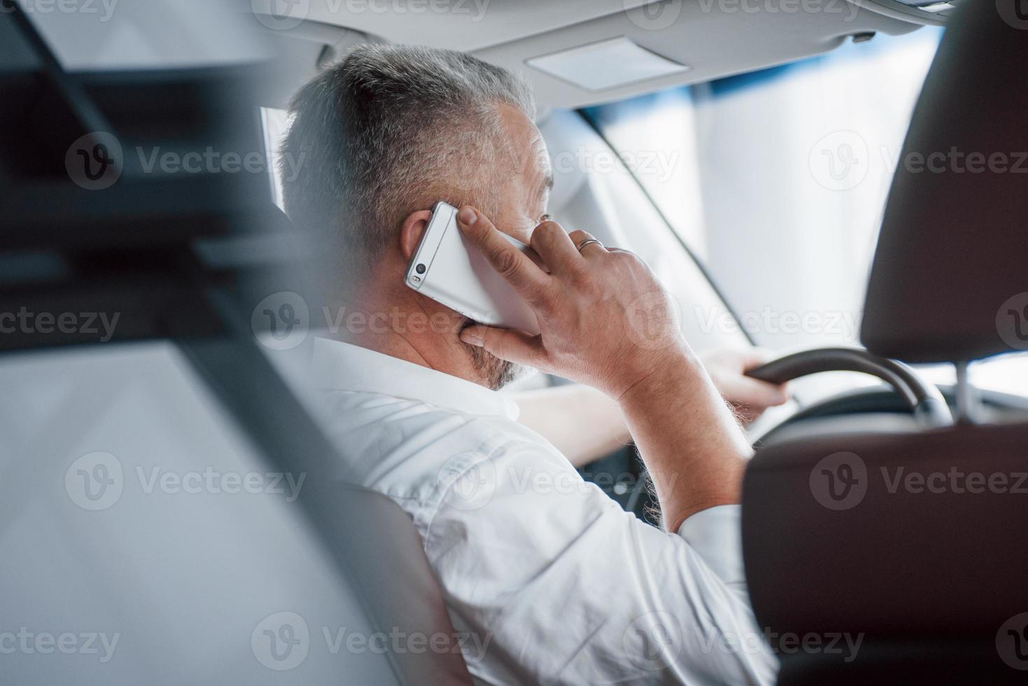 Silver colored phone. Having business call while sitting at the front of modern luxury car photo