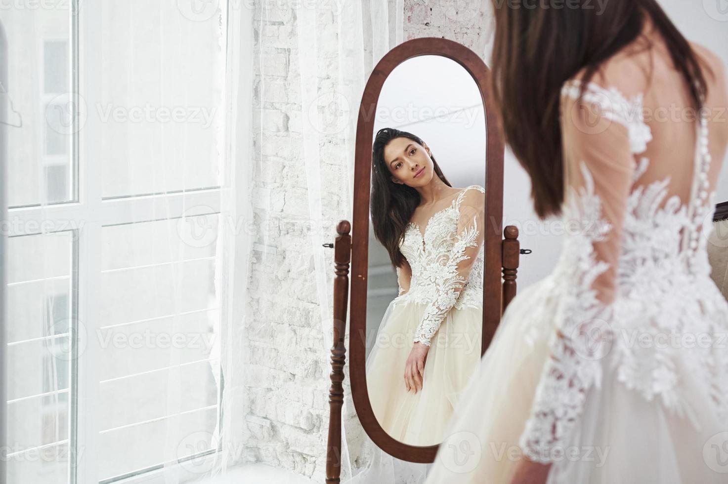 Young bride looks in the mirror. The process of fitting the dress in the studio of hand crafted clothes photo