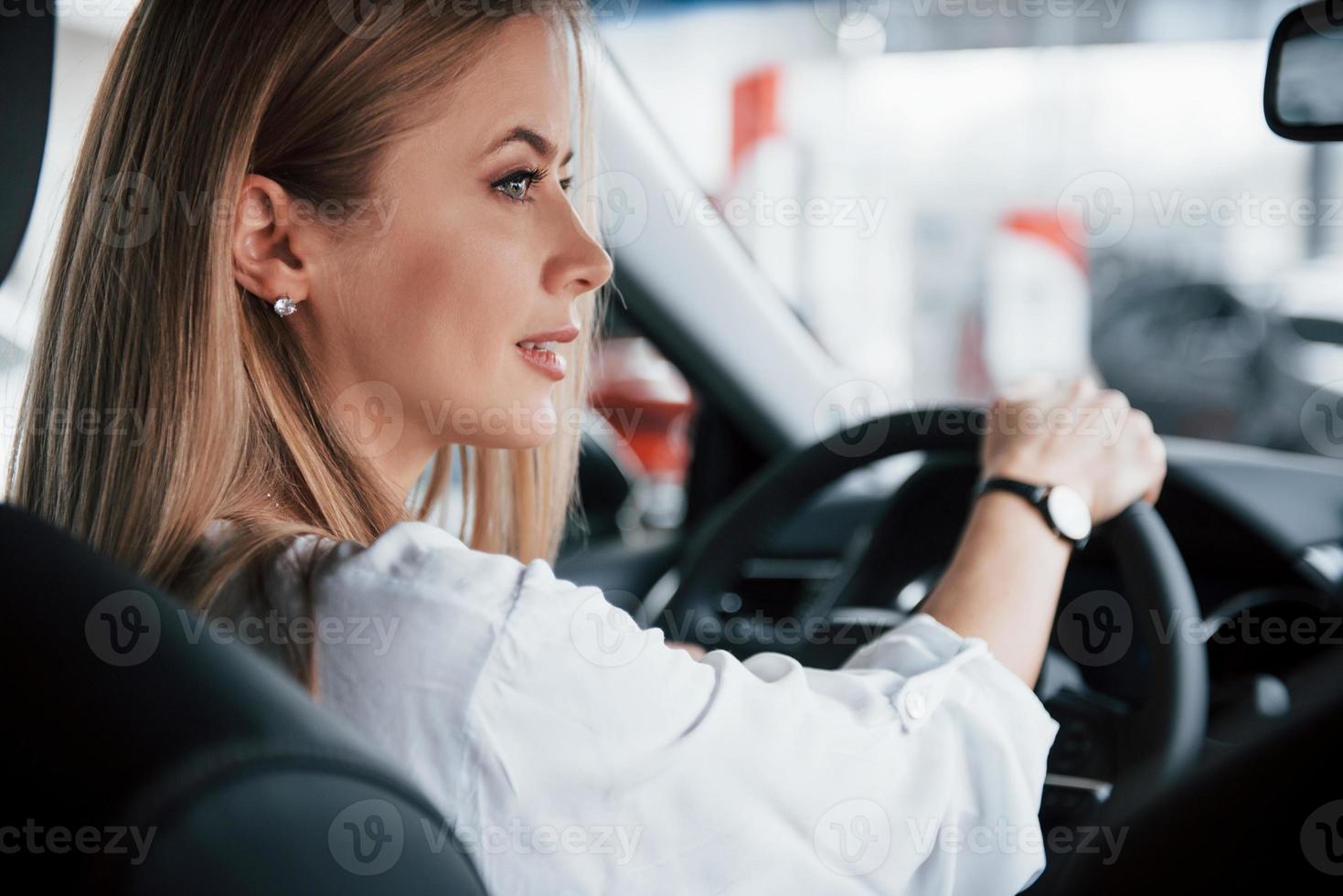 girando a la derecha. hermosa chica rubia sentada en el auto nuevo con interior negro moderno foto