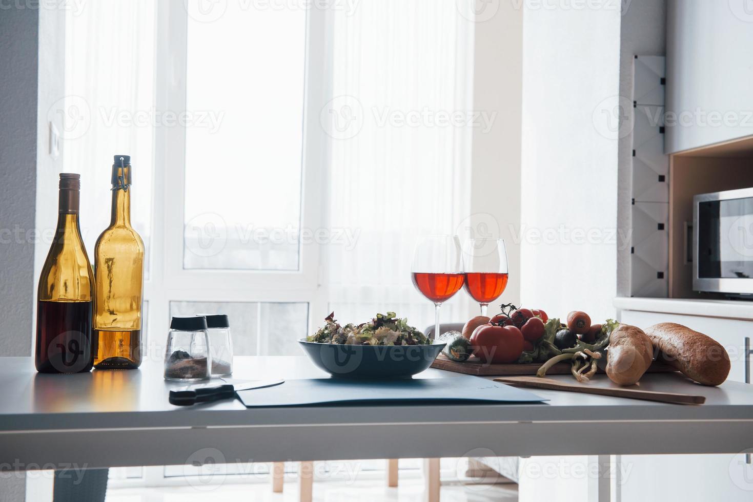 listo para comer. foto de verduras, ensalada y dos vasos con vino tinto en la mesa