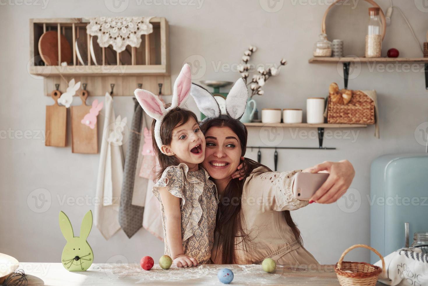 haciendo muecas. madre e hija con orejas de conejo en Semana Santa se divierten en la cocina durante el día foto