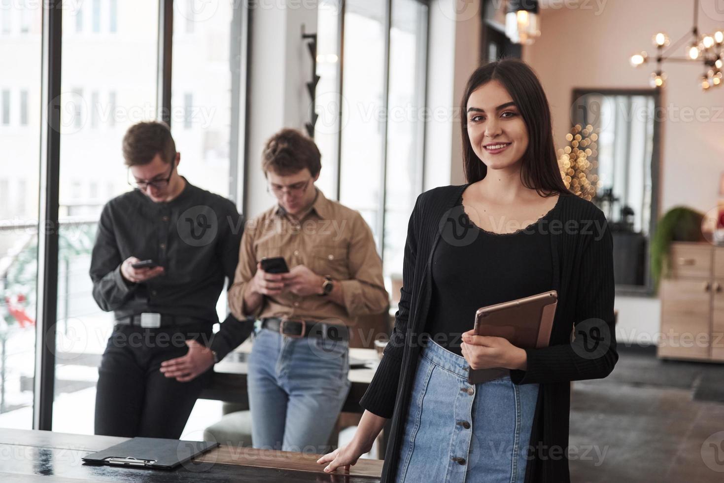 Portrait of woman with tablet in hand. Group of students in eyewear standing in the learning room with documents photo