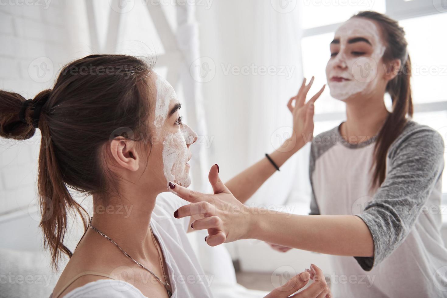 Who needs make up artist when you have friend. Conception of skin care by using white mask on the face. Two female sisters have weekend at bedroom photo