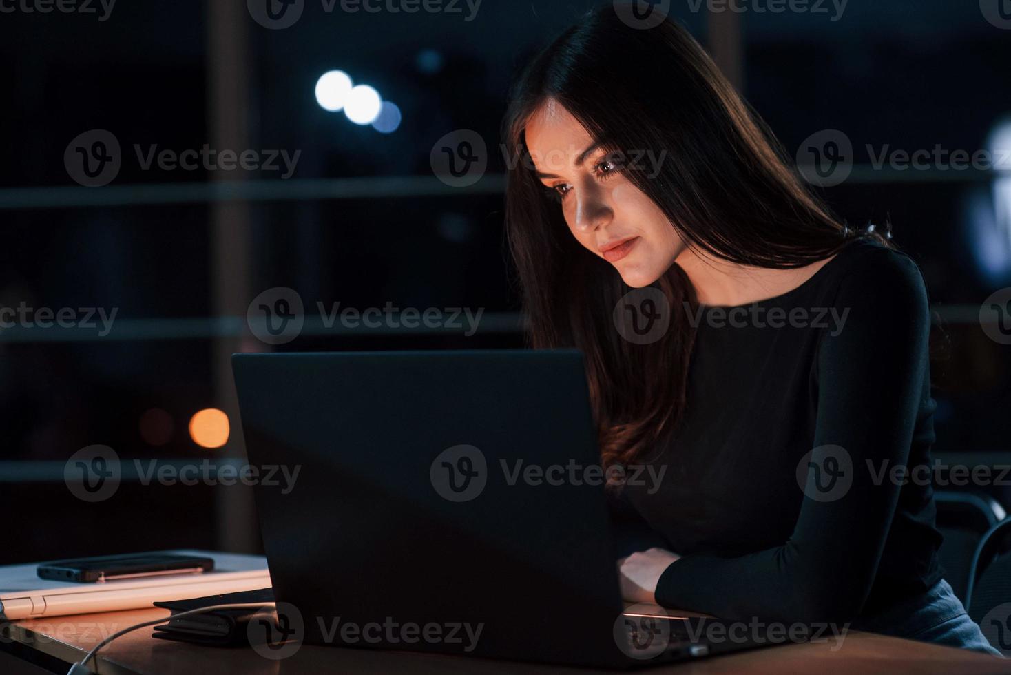 Different digital devices on the table. Attractive brunette businesswoman works alone in the office at nightime photo