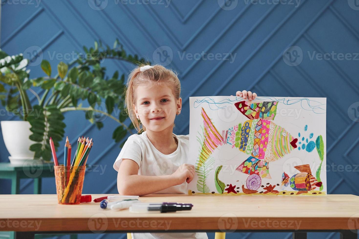Showing off and feeling satisfaction. Cute little girl in art school shows her first paintings drawn by pencils and markers photo