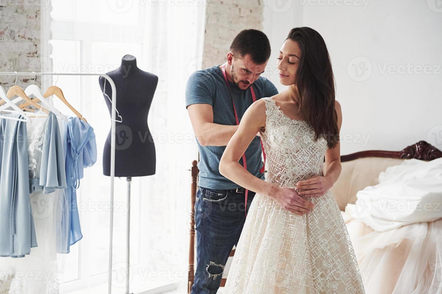 el hombre está ayudando a la novia. el proceso de ajuste del vestido en el estudio de ropa artesanal foto