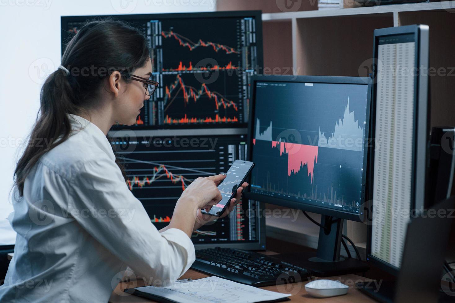 Girl checks new information. Woman working online in the office with multiple computer screens in index charts photo