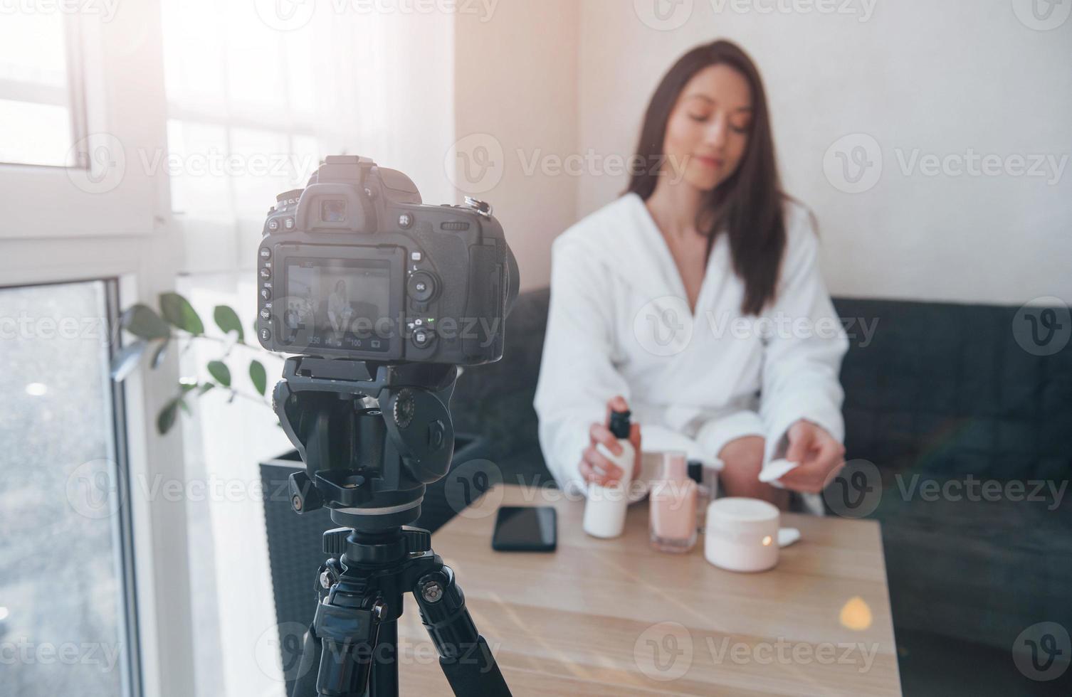 Black professional camera. In front of camera on the tripod. Conception of fashion and skincare. Brunette girl uses cosmetics photo