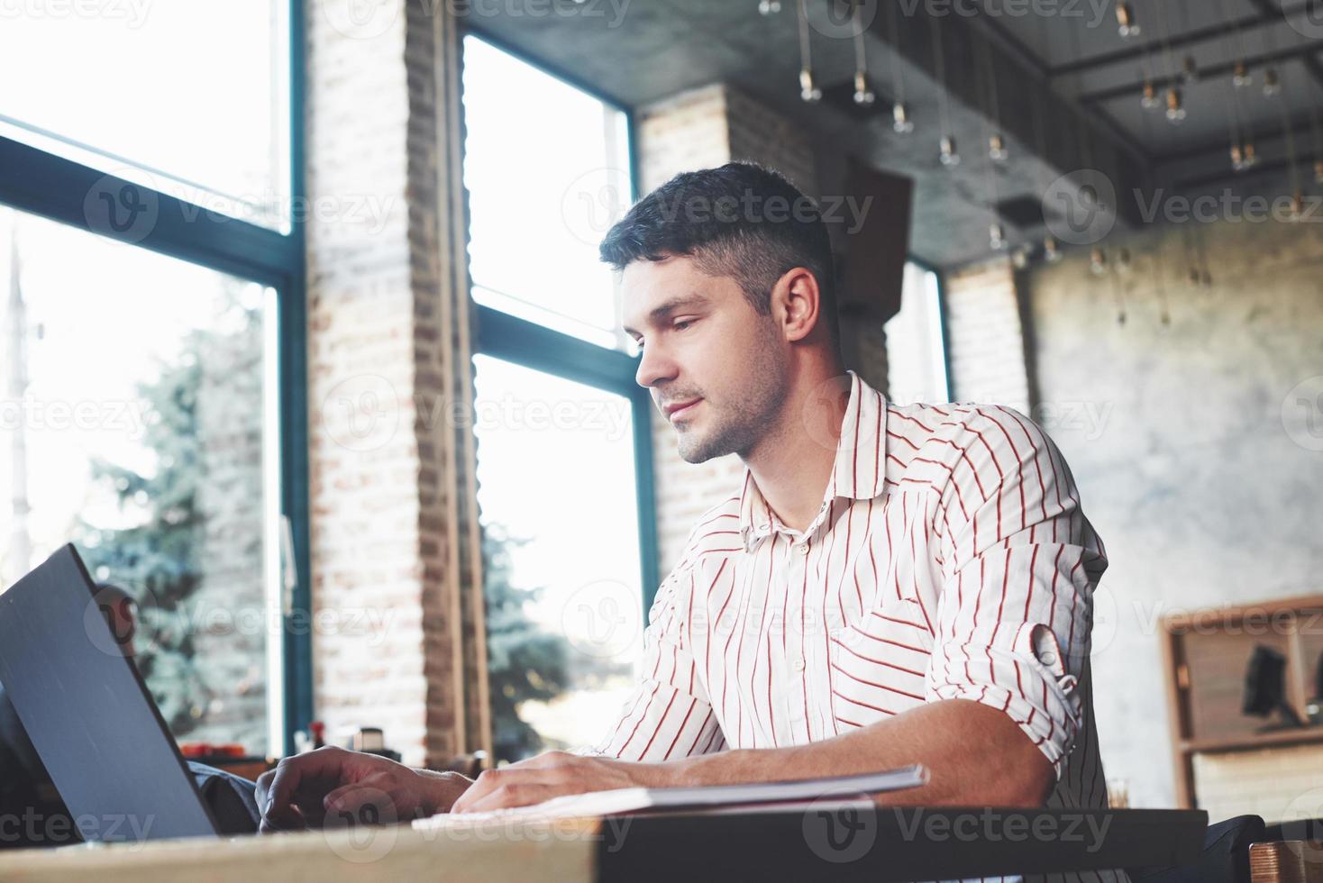 Calm and relaxed. Adult man sits in cafe at daytime and using the laptop for the remote work photo