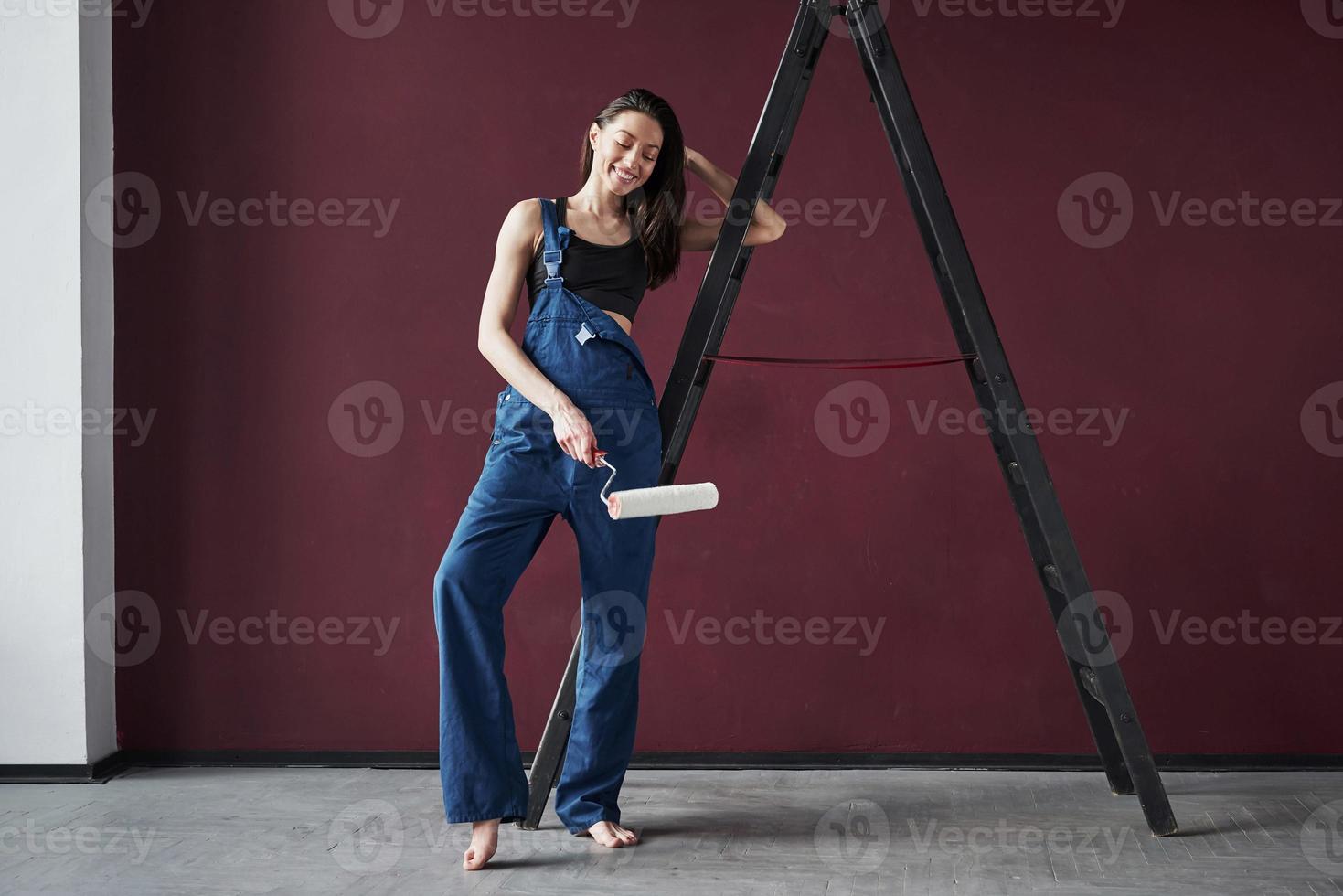Resting by standing near the ladder. Young housewife decided to glue wallpaper in her new house in the room photo