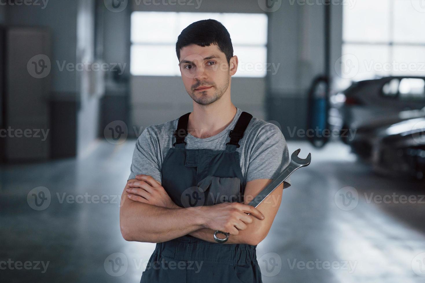 Calm and focused. Portrait of serious worker in uniform that stands in his workshop with wrench in hand photo