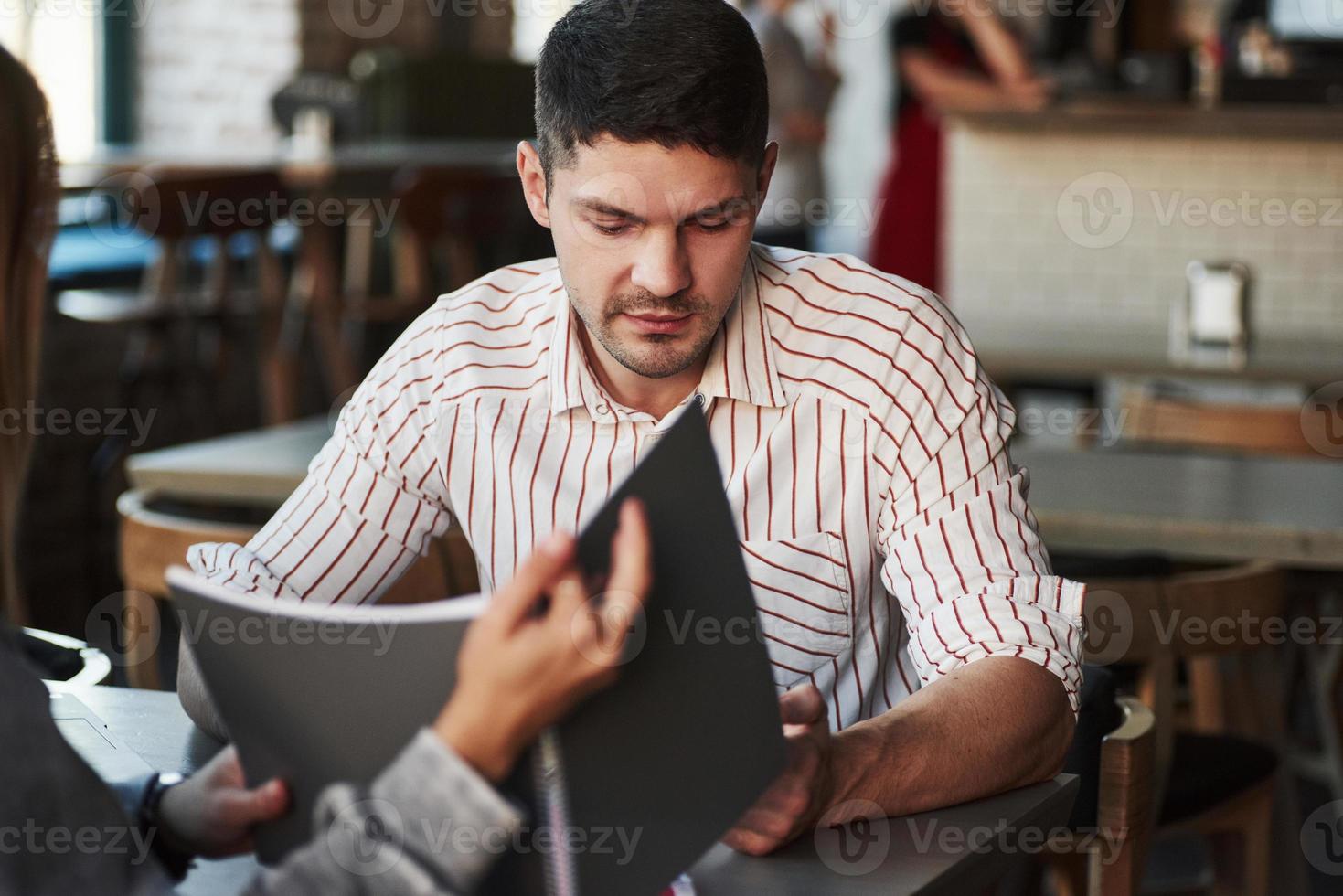 mujer sosteniendo un libro de texto. la gente tiene conversación en el restaurante. hombre con camisa a rayas habla con una chica foto