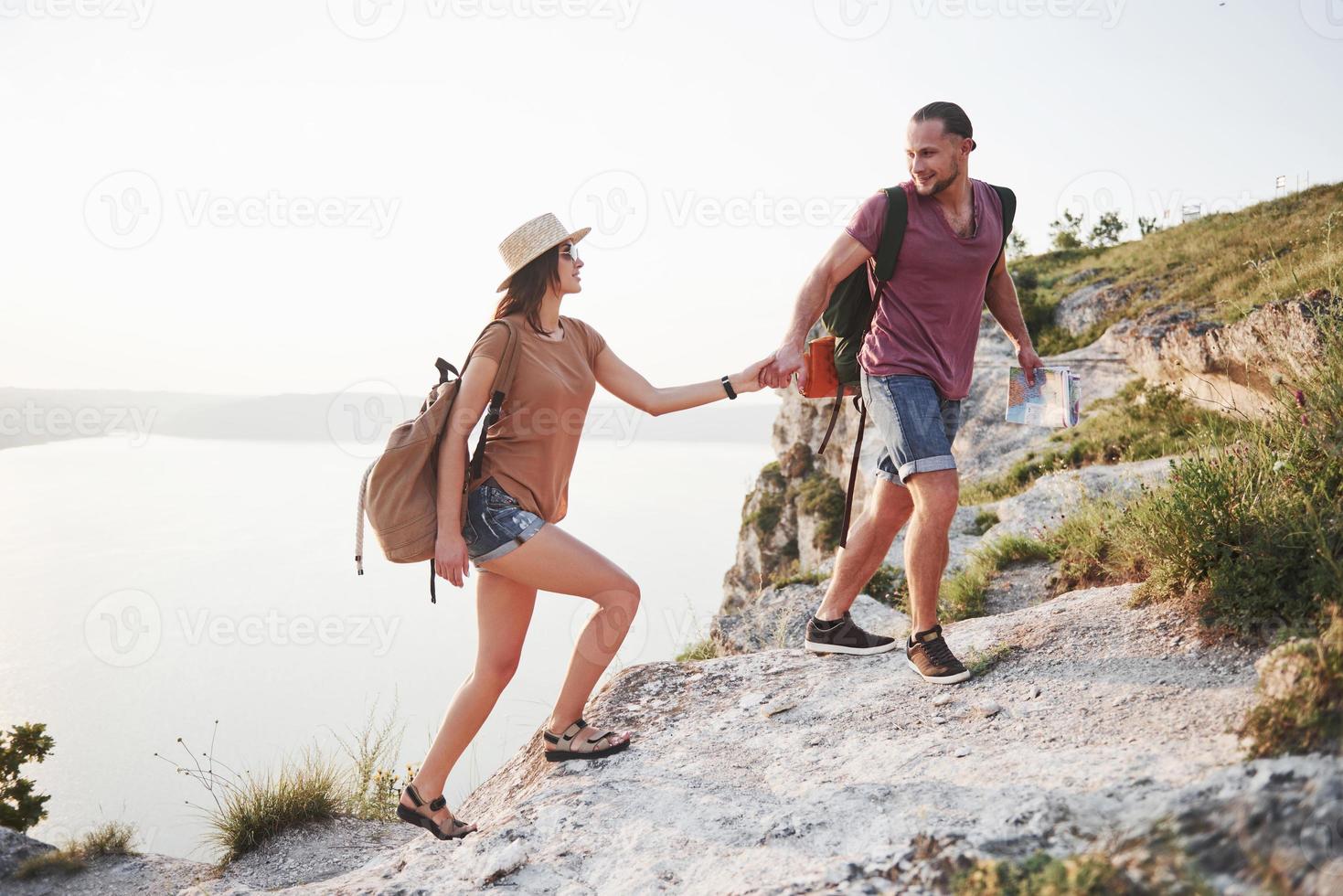 Dos turistas con mochilas suben a la cima de la montaña y disfrutan del amanecer. foto