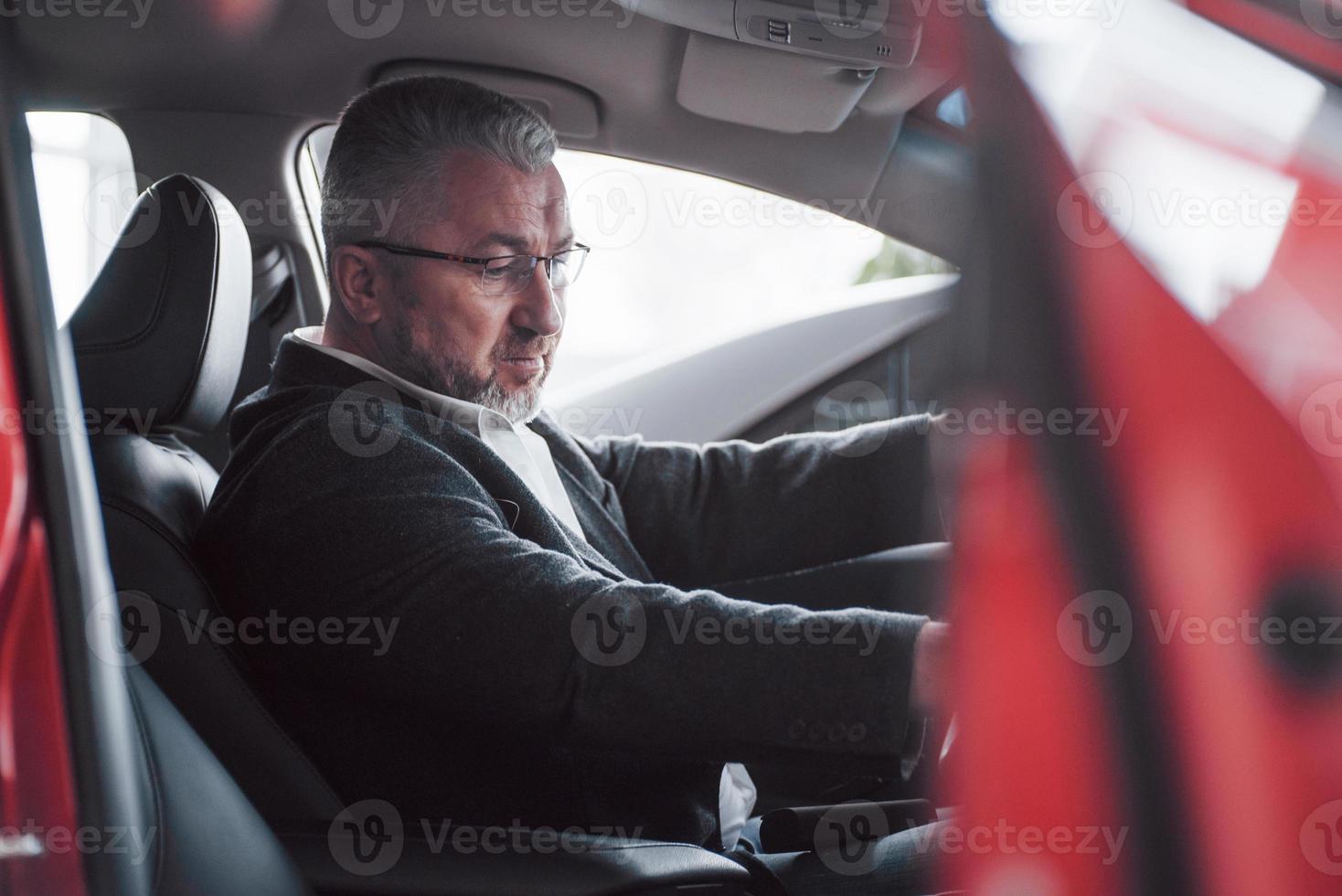 Trying new functions. Side view of senior businessman in official clothes driving a modern new car photo