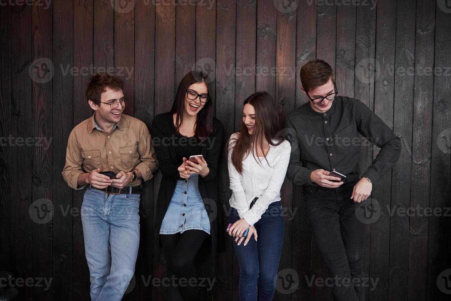 Girl swows funny joke. Youth stands against black wooden wall. Group of friends spending time together photo