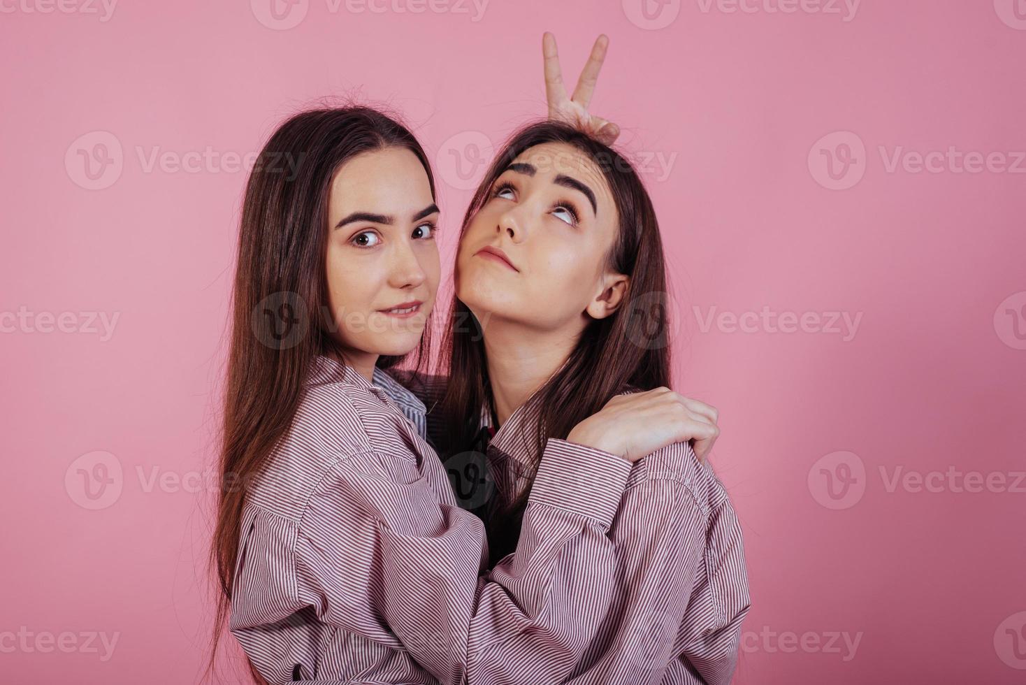 perder el tiempo. dos hermanas gemelas de pie y posando en el estudio con fondo rosa foto