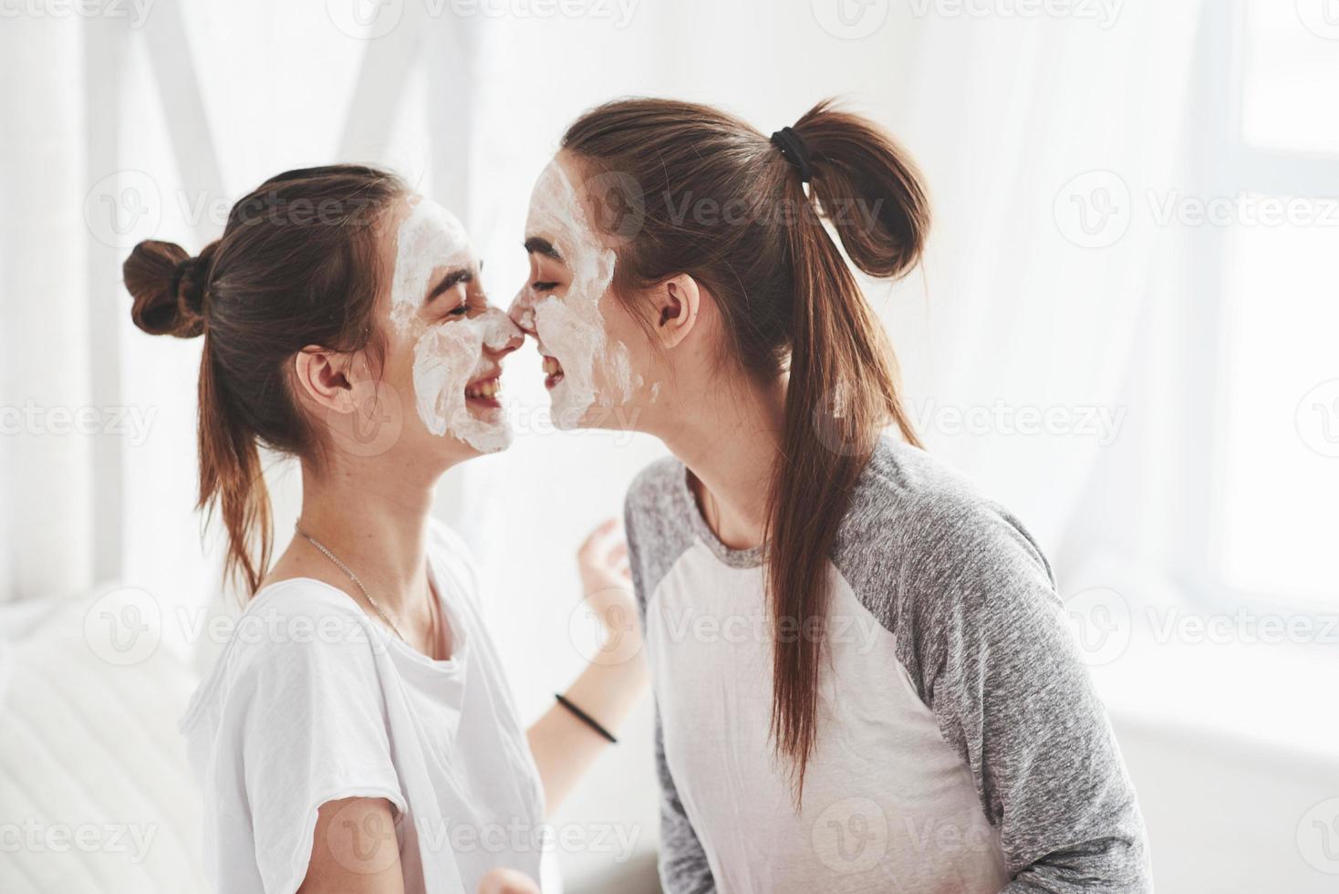 Playing like kinds again. Conception of skin care by using white mask on the face. Two female sisters have weekend at bedroom photo