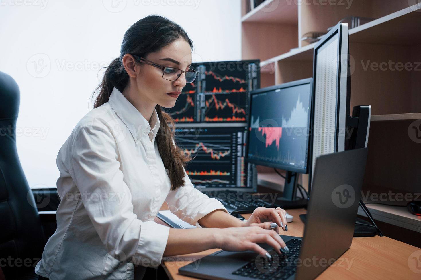 escribiendo en la computadora portátil. mujer que trabaja en línea en la oficina con múltiples pantallas de computadora en gráficos de índice foto