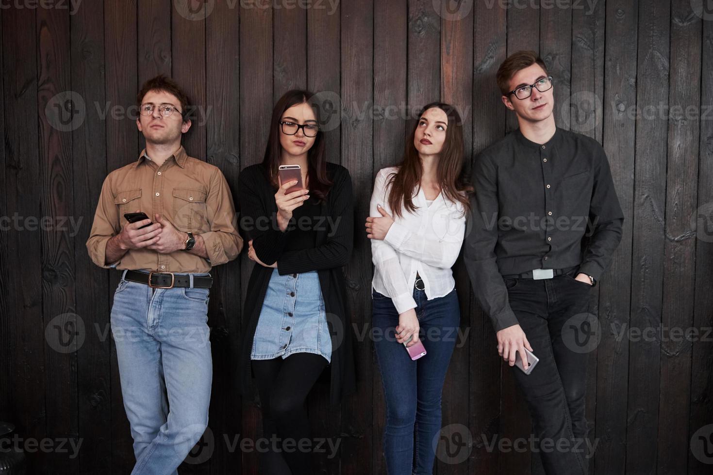 Thoughtful looks. Youth stands against black wooden wall. Group of friends spending time together photo