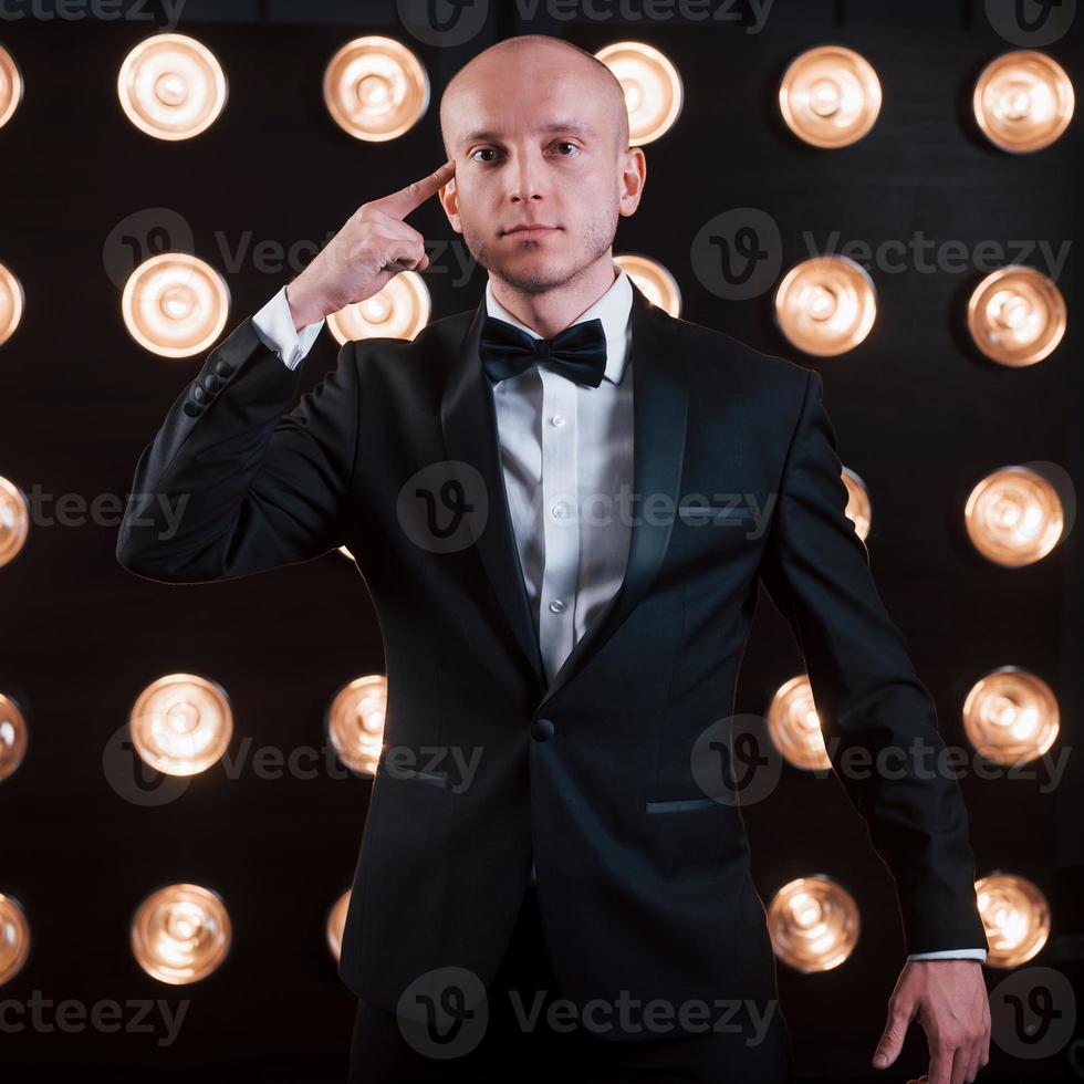 Trying to read your mind. Magician in black suit standing in the room with special lighting at backstage photo