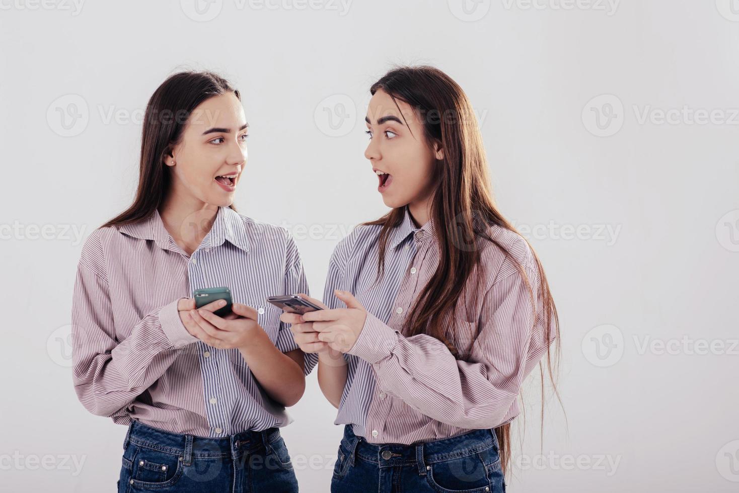 Esa última noticia es increíble. dos hermanas gemelas de pie y posando en el estudio con fondo blanco foto