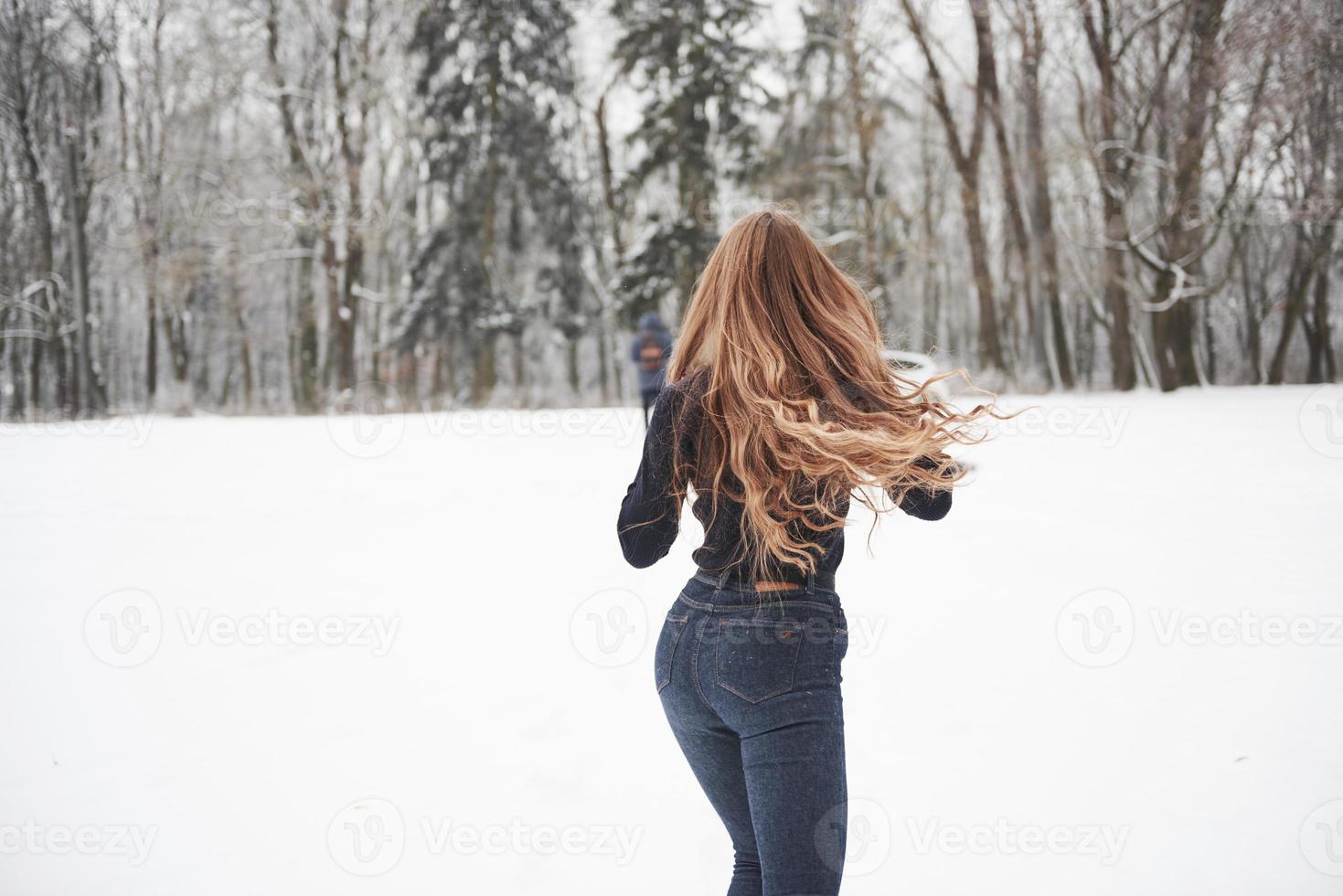 Over there, where our car is. Rear view of girl with long hair runs near the forest to the automobile in wintertime photo
